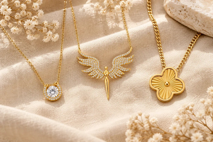 Glücksbringer Schmuck in Gold: Hufeisen-Kette, Schutzengel-Kette und Kleeblatt-Kette auf beigem Leinen