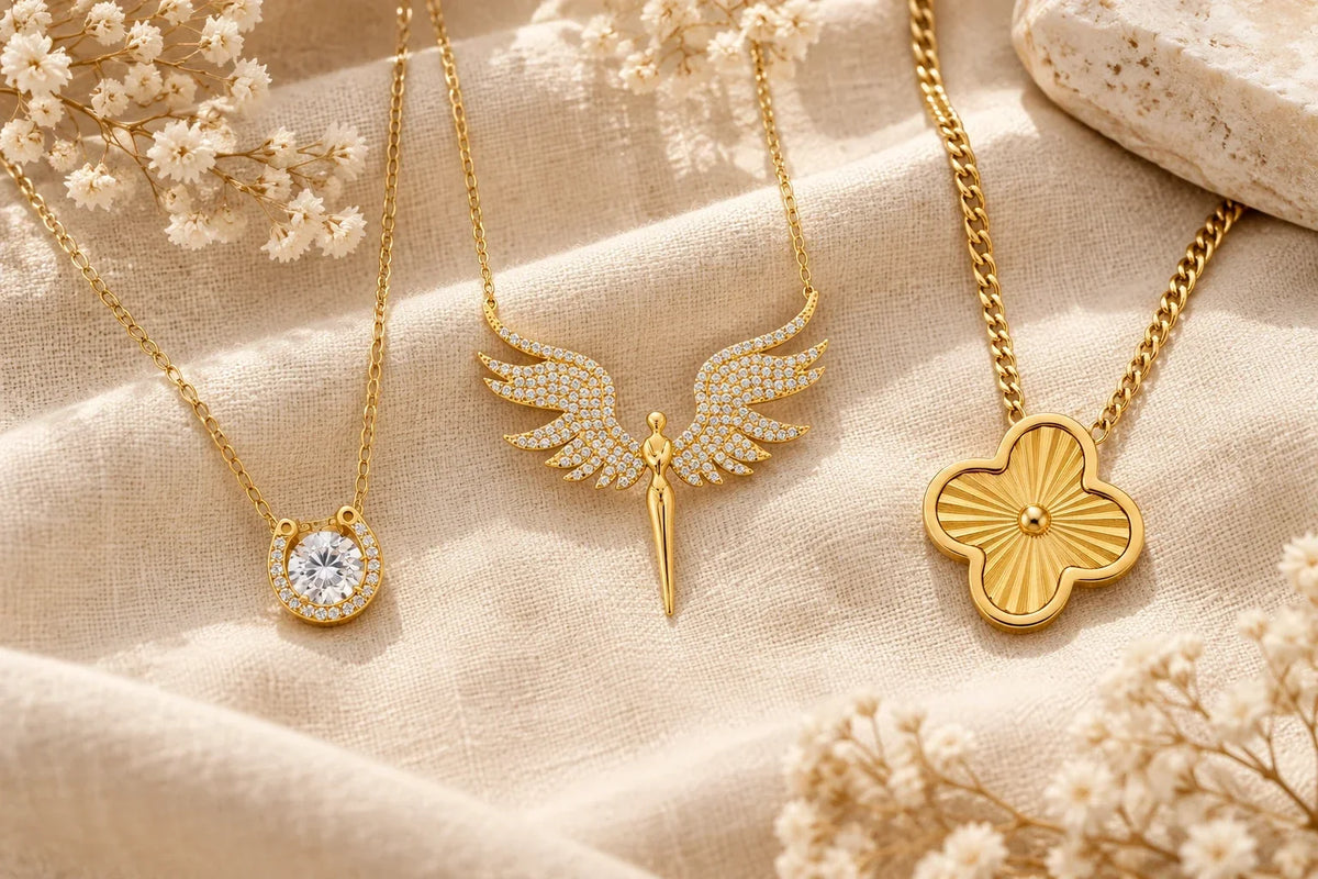 Glücksbringer Schmuck in Gold: Hufeisen-Kette, Schutzengel-Kette und Kleeblatt-Kette auf beigem Leinen