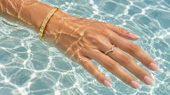 Vergoldeter Armreif und Ring mit Steinen an der Hand im Poolwasser