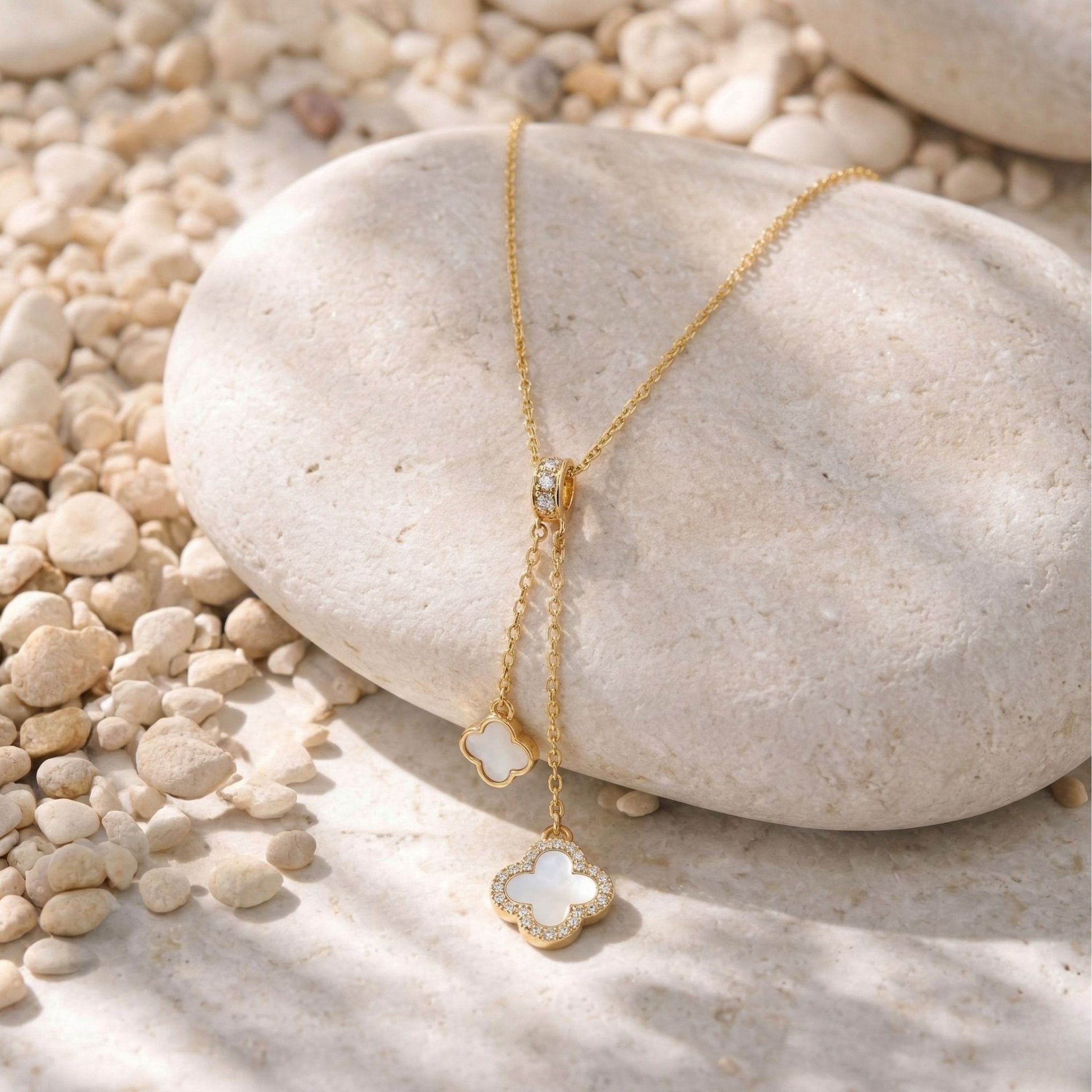 18K Gold Lariat Halskette mit Diamanten und Perlmutt Kleeblatt Anhängern, luxuriöser Goldschmuck freigestellt auf einem hellen Stein