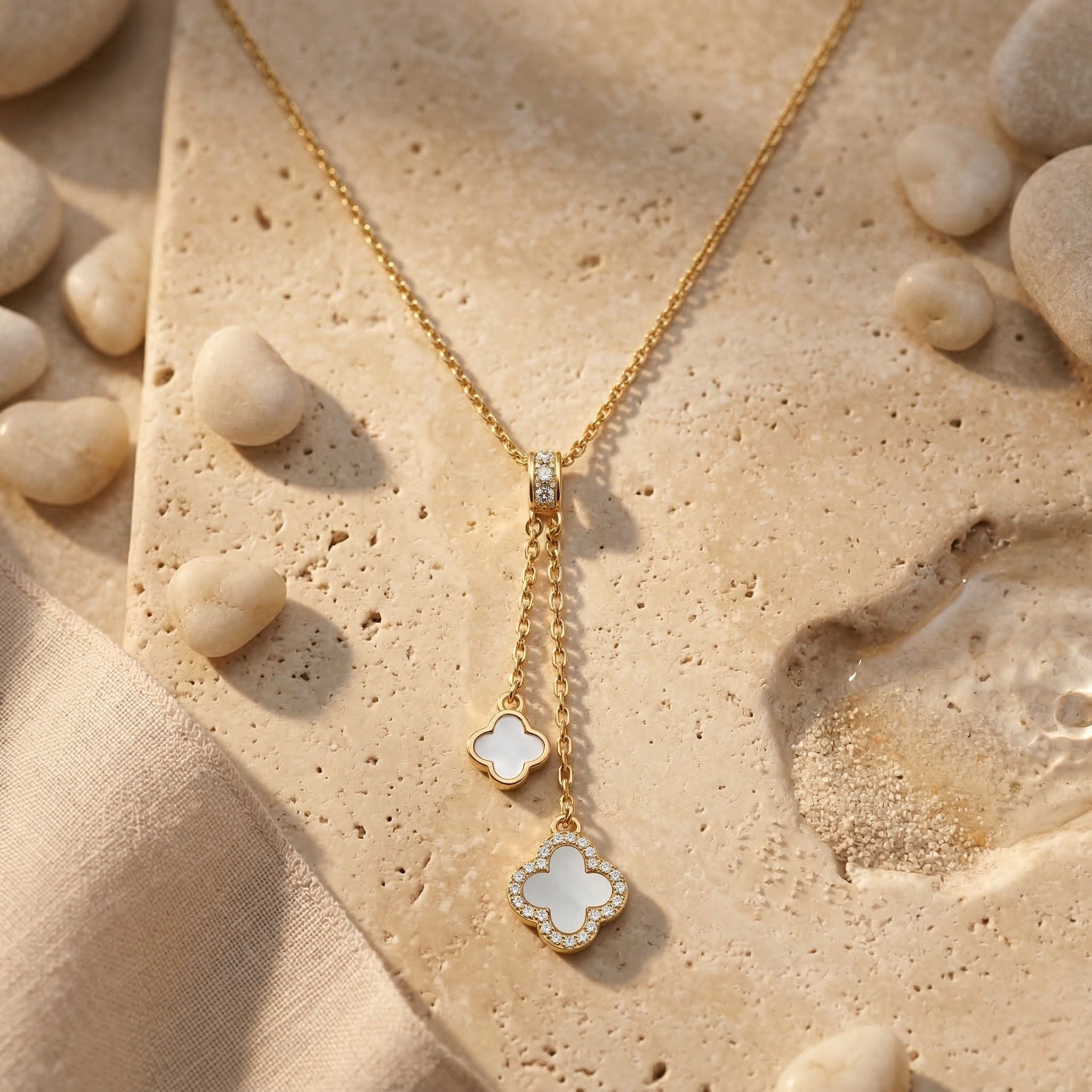 18K Gold Lariat Halskette mit Diamanten und Perlmutt Kleeblatt Anhängern, luxuriöser Goldschmuck freigestellt auf einem hellen Stein