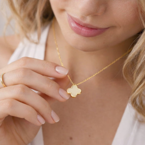 Nahaufnahme einer eleganten Frau, die eine filigrane goldene Halskette mit einem weißen Kleeblatt-Anhänger trägt. Hochwertiger Goldschmuck für Damen und zeitlose Accessoires für einen edlen Look.