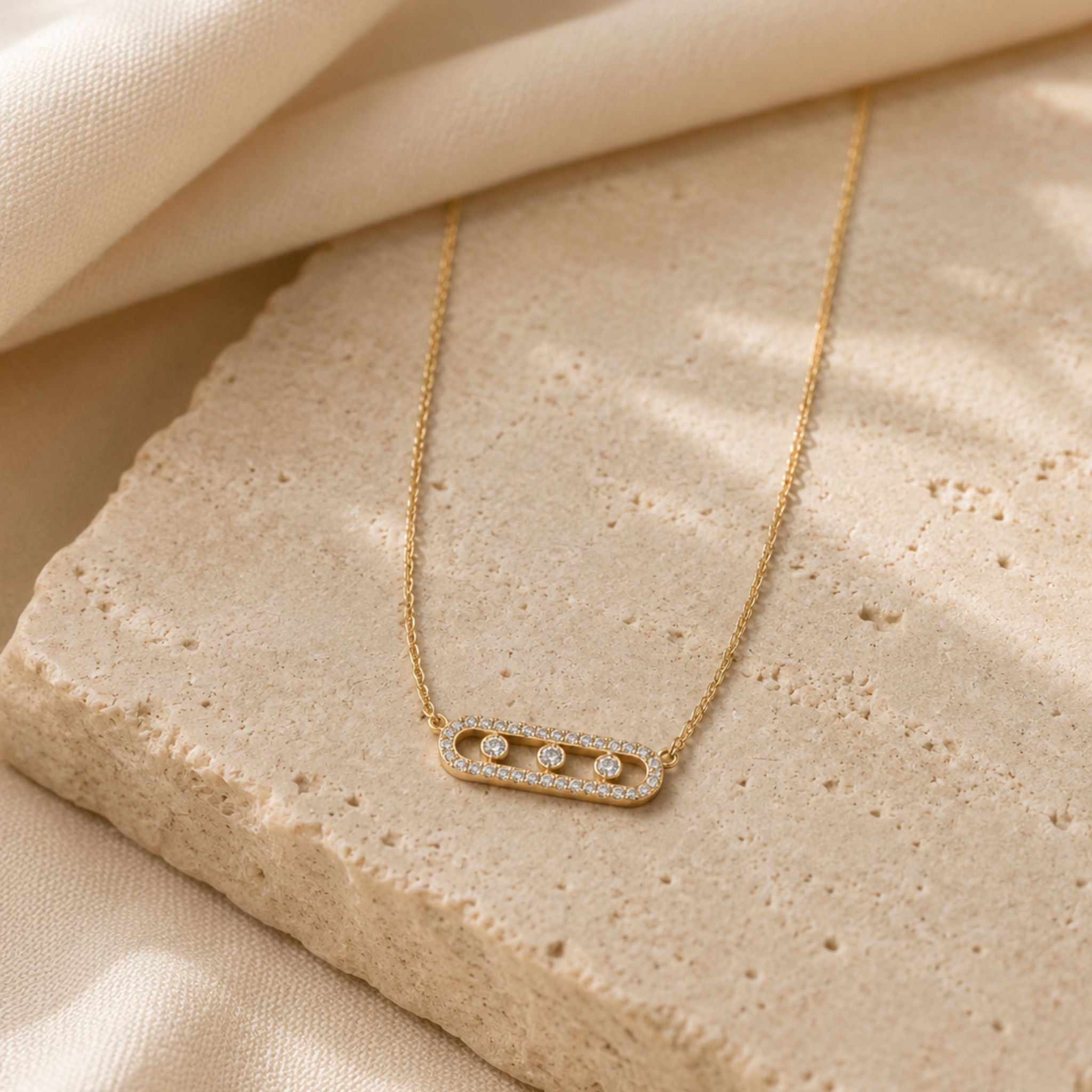 Goldene Trinity Shine Kette mit Zirkonia auf hellem Naturstein präsentiert