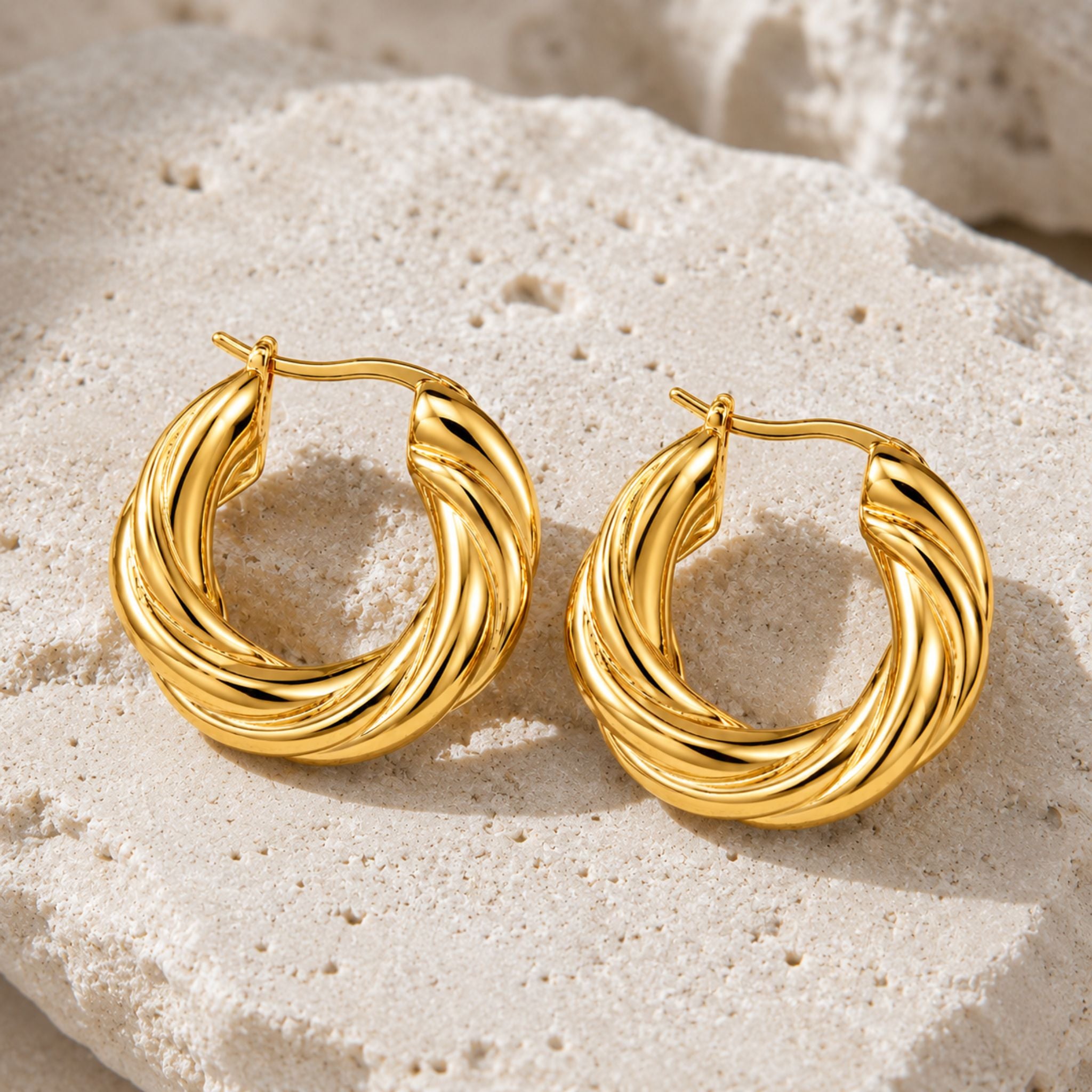 Goldene Twisted Hoop Ohrringe auf hellem Naturstein präsentiert