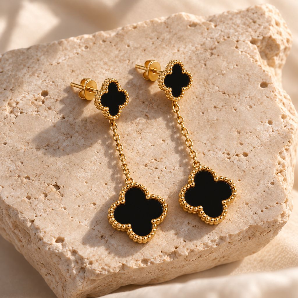 Schwarze Kleeblatt-Ohrhänger in Gold auf hellem Naturstein, wasserfester Schmuck aus Edelstahl